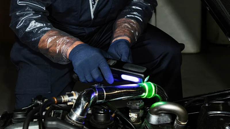 Illustreret UV-lampe over rør og samlinger med gulgrønt farvespor ved en lækage